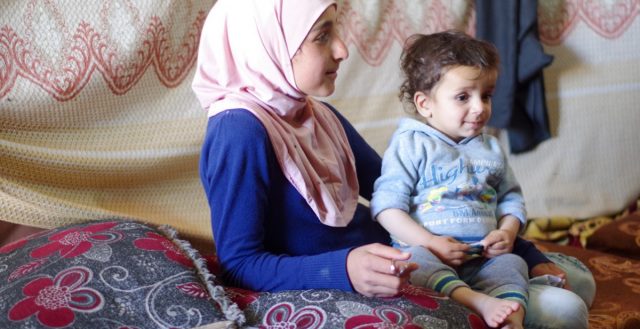 Syrian refugee girl caring for her brother whilst others play. Photo: Ingrid Gercama/GAGE