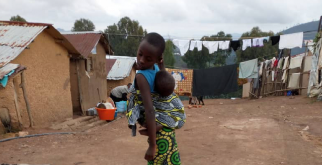 Adolescent girl carrying her sibling on her back while selling charcoal in Gihembe refugee camp, Northern Province, Rwanda. Photo: Simpunga Manzi Didier